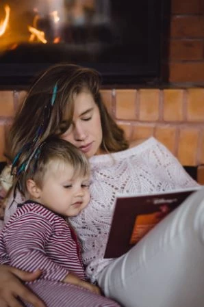 Mother reading to her son in front of a wood fireplace